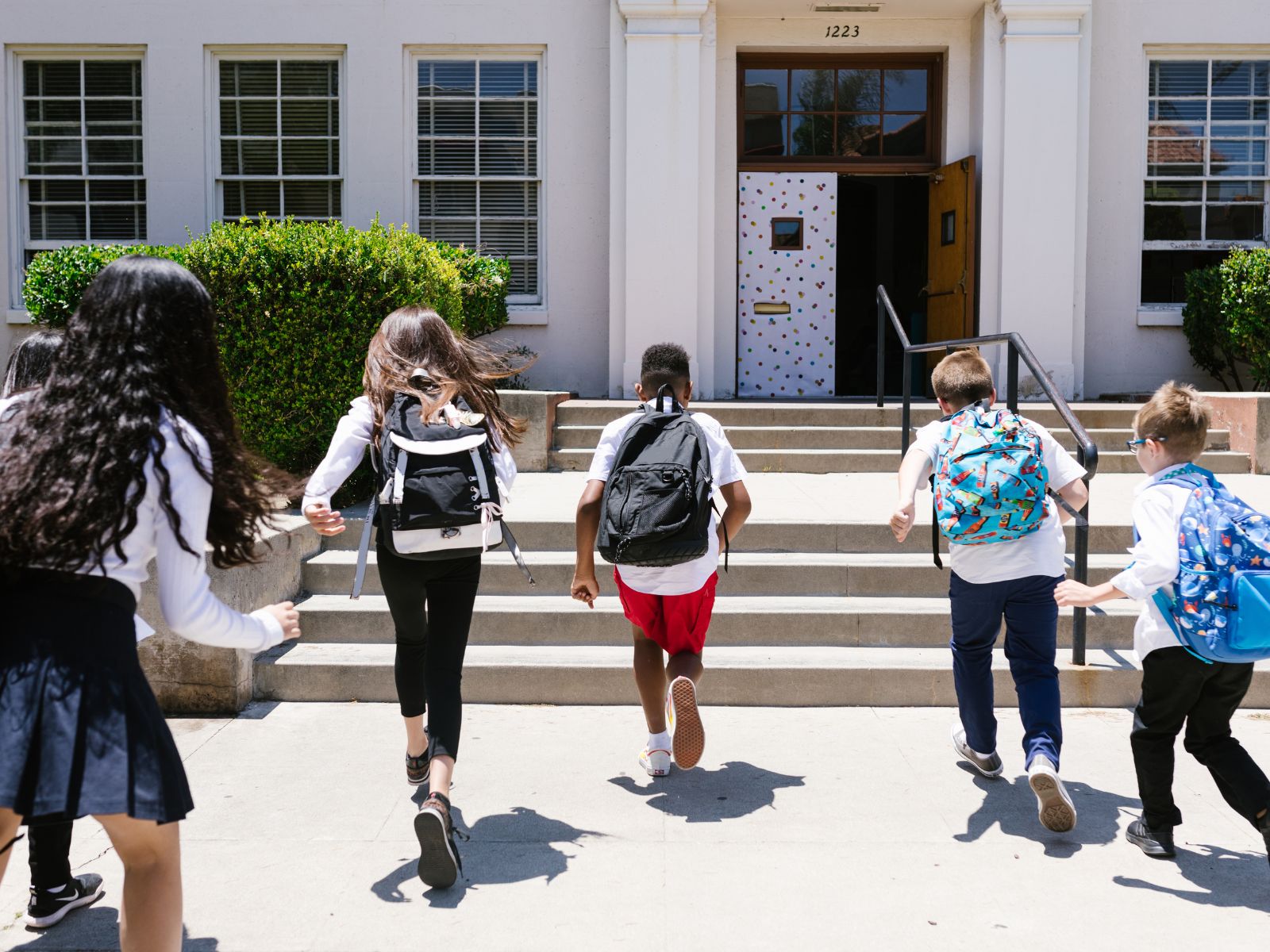 Students running to school entrance with backpacks, ideal for scholastic achievement awards and school events.