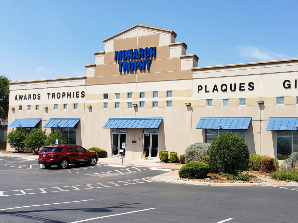 Monarch Trophy storefront with blue awnings, offering awards, trophies, and plaques under clear skies.
