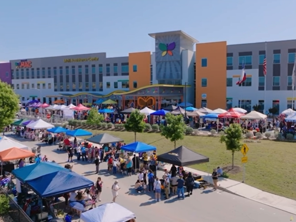 Outdoor community event with colorful vendor tents and crowds gathered in front of a modern building