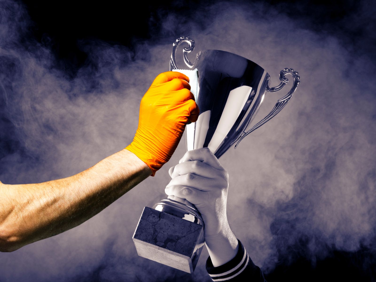 Hand polishing a shiny silver trophy with ornate handles against smoky background